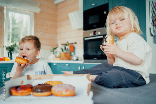 Children eat sweet doughnuts with sugar in the kitchen.