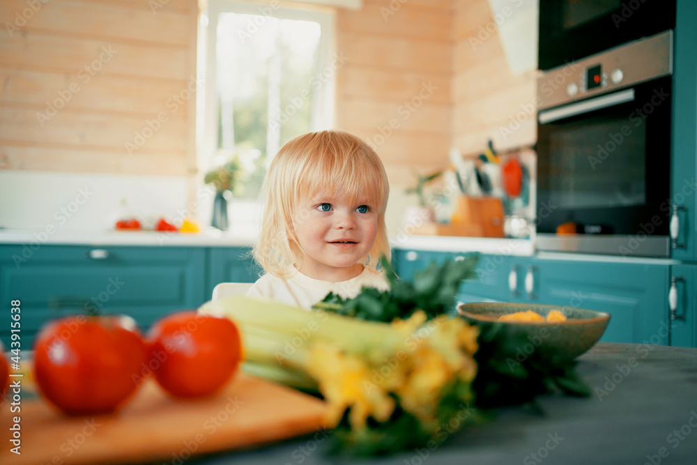 A small blonde child is playing in the kitchen in the apartment. Eats fresh vegetables for a healthy breakfast. A cheerful child's mood has a fascinating time. A small blonde child is playing in the kitchen in the apartment. Eats fresh vegetables for a healthy breakfast. A cheerful child's mood has a fascinating time.