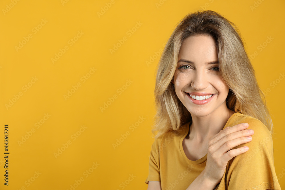 Fototapeta premium Portrait of happy young woman with beautiful blonde hair and charming smile on yellow background. Space for text