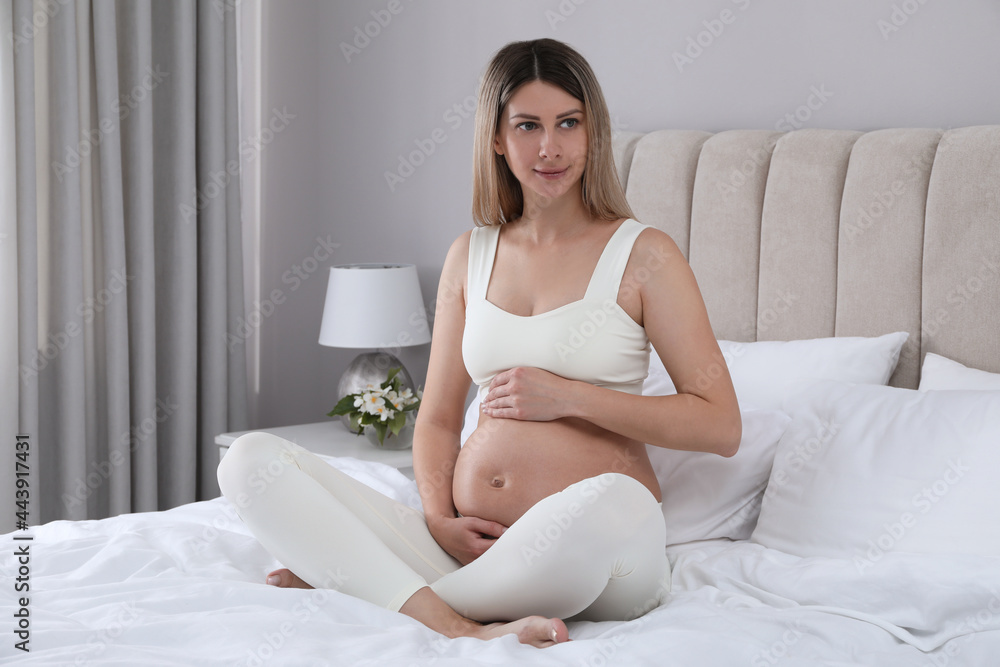 Beautiful pregnant woman sitting on bed at home Beautiful pregnant woman sitting on bed at home