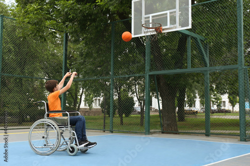 Disabled teenage boy in wheelchair playing basketball  on outdoor court