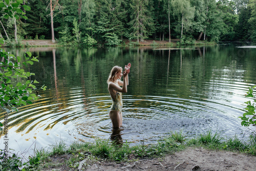 Cheerful young woman splashing water of lake in picturesque forest