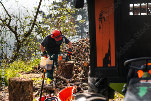 Lumberman fueling chainsaw during work at sawmill 