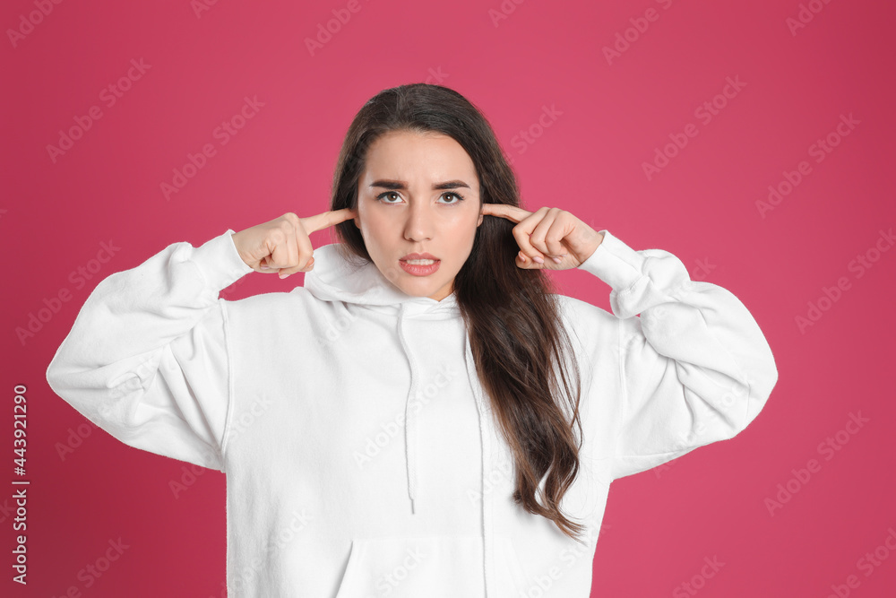 Young woman covering ears with fingers on pink background Young woman covering ears with fingers on pink background