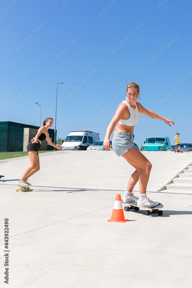 Happy girls riding a surf skate around traffic cones Happy girls riding a surf skate around traffic cones