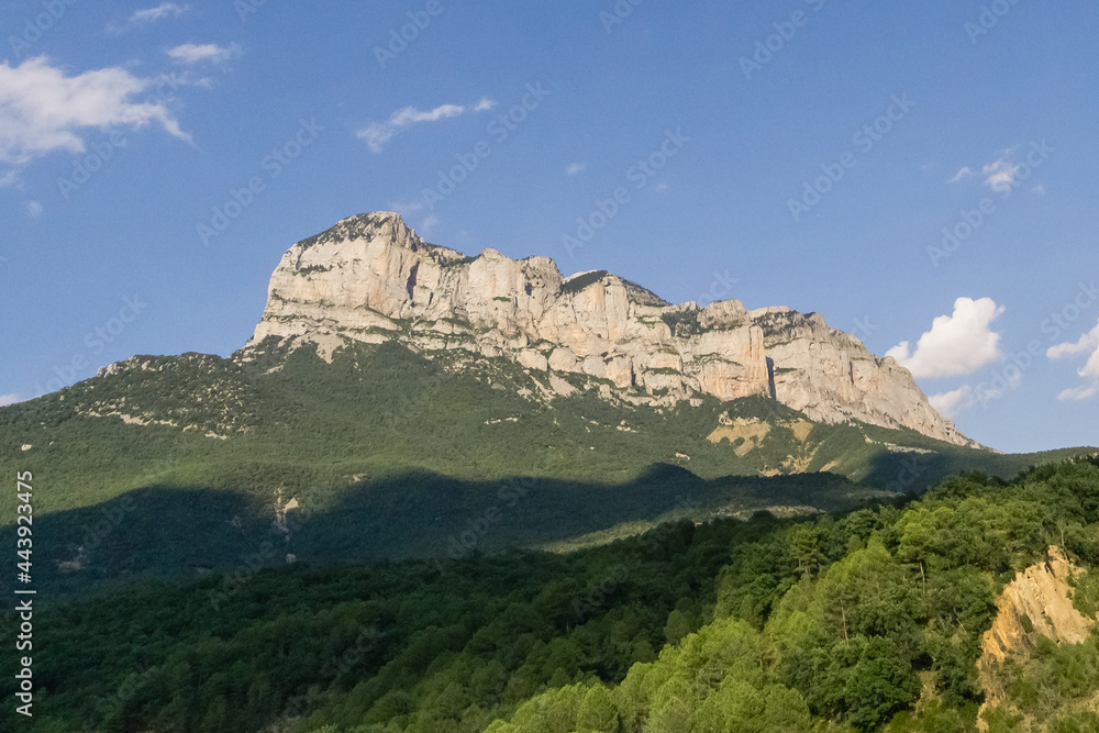 Rock formation in pyrenees under blue summer sky with green forest in foreground