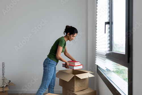 Young woman unpacking a moving box with books photo