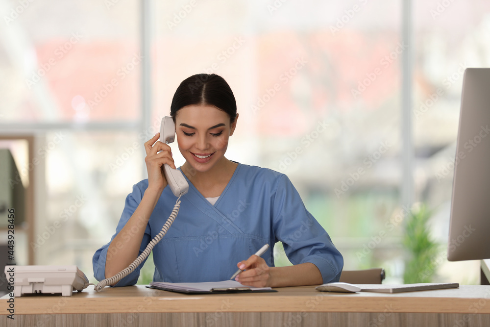 Receptionist talking on phone at countertop in hospital - obrazy, fototapety, plakaty 