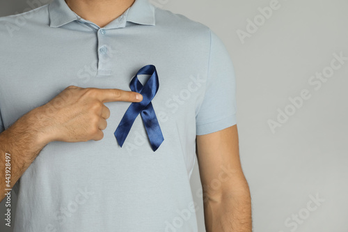 Man with blue ribbon on grey background, closeup. Urology cancer awareness