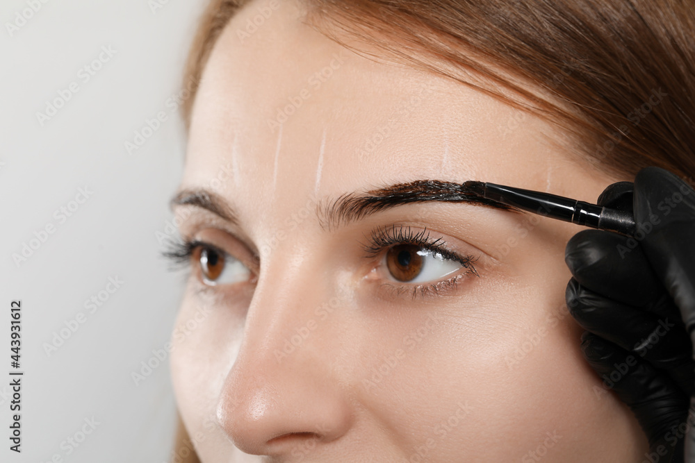 Beautician applying tint during eyebrows correction procedure on grey background, closeup Beautician applying tint during eyebrows correction procedure on grey background, closeup