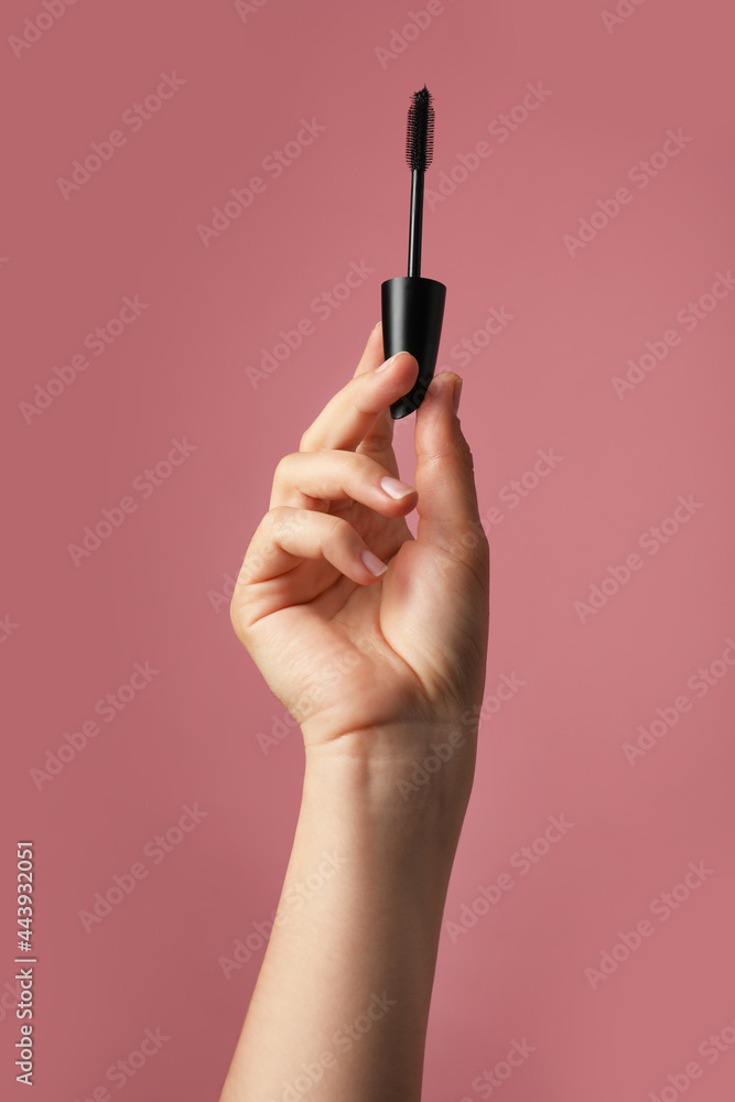 Woman holding mascara for eyelashes on dusty rose background, closeup Woman holding mascara for eyelashes on dusty rose background, closeup