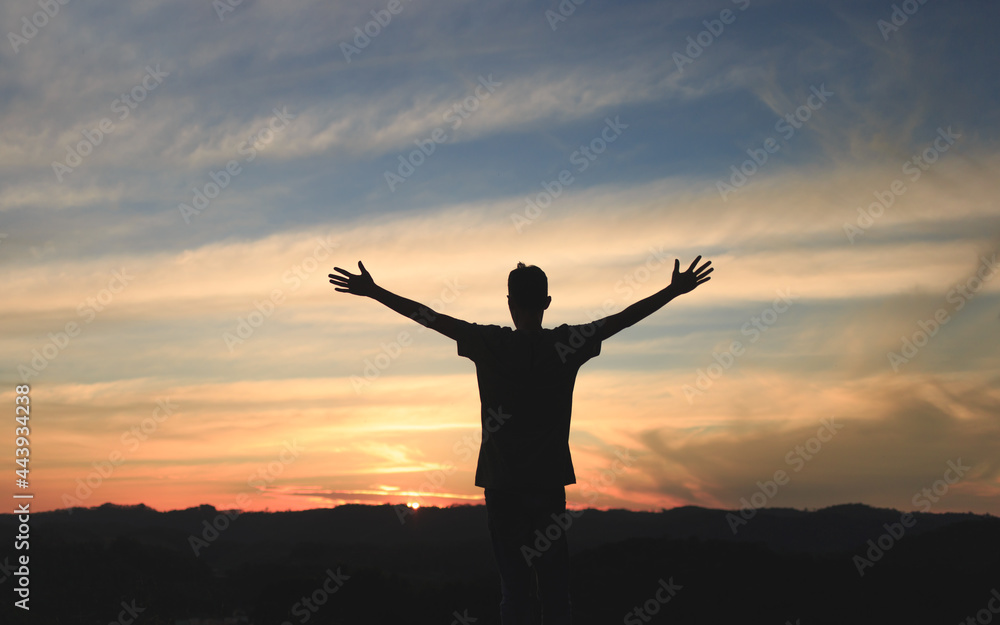 Silhouette of a man with open arms, with sky after sunset and mountains in the background. Freedom, happiness, faith and gratitude concept.