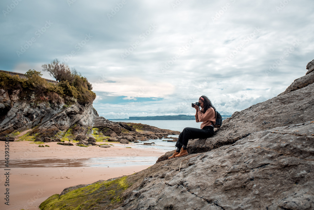 Young female photographer taking picture of sea sitting on rocky boulder Young female photographer taking picture of sea sitting on rocky boulder