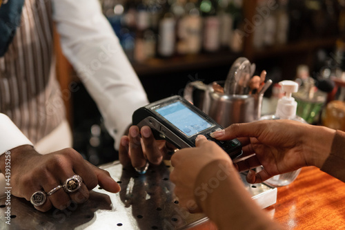 Crop black woman entering pin code into terminal in bar photo