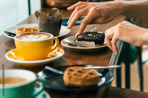 Young woman' s hand over a plate of cake, smartphone on the table. In the foreground is a cup of coffee
