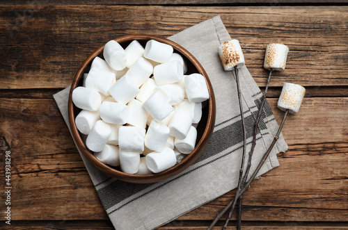Sticks with roasted marshmallows on wooden table, flat lay