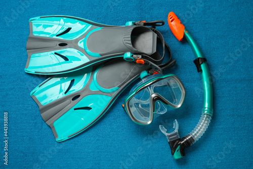 Pair of turquoise flippers and mask on blue fabric, flat lay