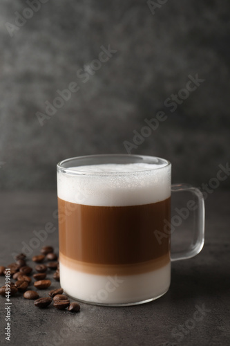 Hot coffee with milk in glass cup and beans on grey table
