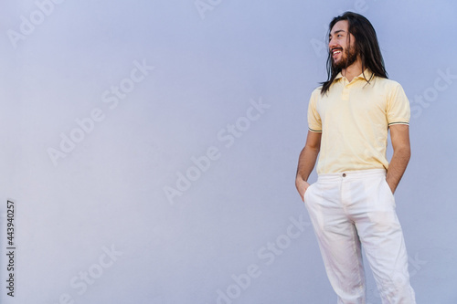 young hispanic latino male with long hair, college student looking away while laughing, copy space, grey wall background