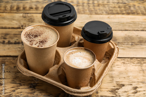 Takeaway paper coffee cups in cardboard holder on wooden table