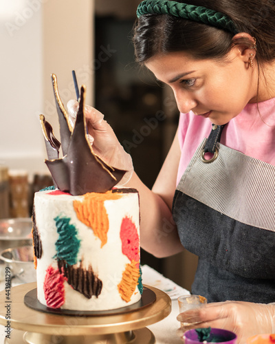 Young woman concentrating on decorating a cake with buttercream in a large kitchen.