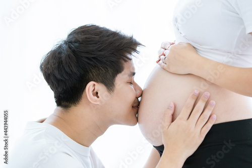 Happy Asian family, cheerful husband tenderly kissing on his wife's stomach, wife is pregnancy.