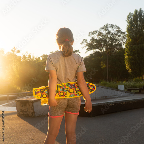 a girl stands with a skateboard in her hands. the child goes in for sports. beautiful girl in the sun