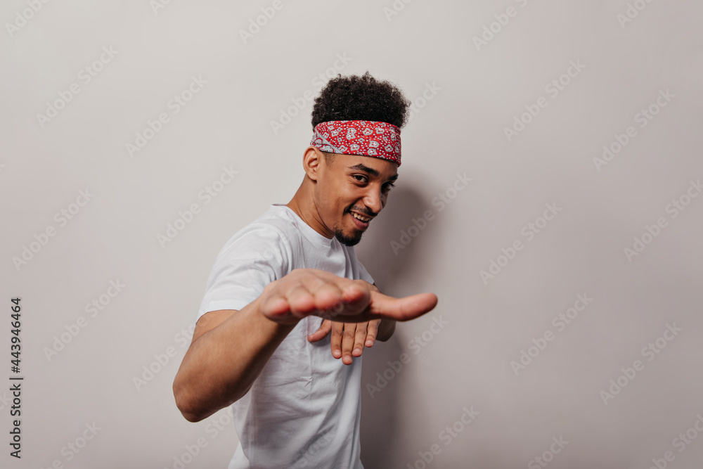 Man in red bandana and white t-shirt is having fun on isolated background. Cheerful dark-skinned guy in tee looking into camera and smiling Man in red bandana and white t-shirt is having fun on isolated background. Cheerful dark-skinned guy in tee looking into camera and smiling