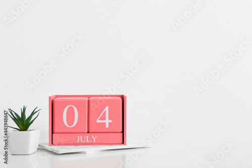 Cube calendar with date JULY 4, houseplant and notebooks on light background