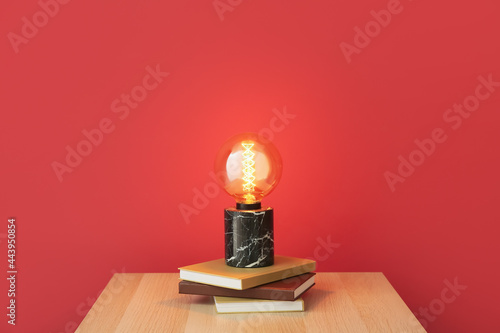 Glowing lamp and books on table near color wall