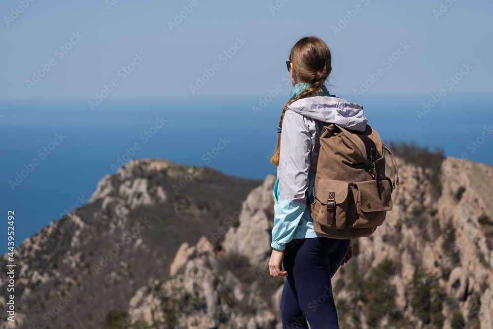 A woman traveler with a large hiking backpack climbed a high mountain and enjoys a beautiful view. Inspirational travel. Love of adventure.