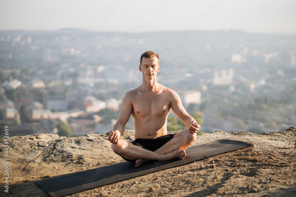 Peaceful shirtless man sitting on yoga mat and practicing lotus pose with closed eyes. Concept of people, sport activity and nature.