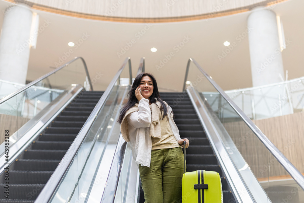 Beautiful lady tourist going down with baggage on escalator at terminal of international airport Beautiful lady tourist going down with baggage on escalator at terminal of international airport