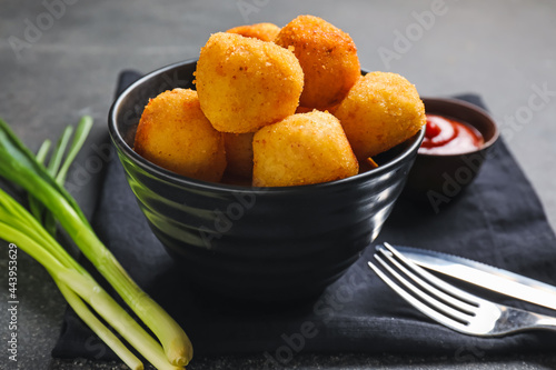 Bowl with fried potato balls on dark background