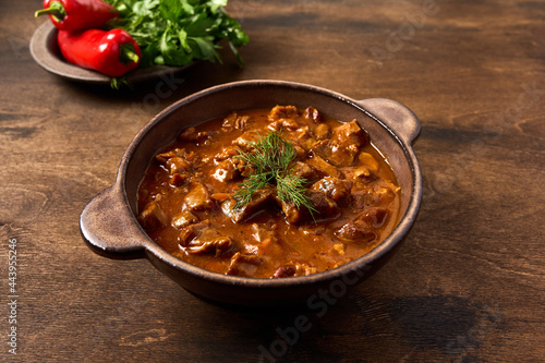 Traditional goulash meat in ceramic bowl on wooden brown background with pepper and herbs. Close up photo