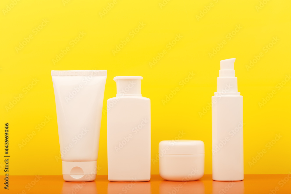 Set of white unbranded cosmetic bottles against yellow background. Concept of safe tanning, summer skin care and beauty products for skin with Spf sunscreen Set of white unbranded cosmetic bottles against yellow background. Concept of safe tanning, summer skin care and beauty products for skin with Spf sunscreen