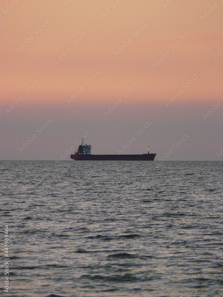 The ships are in the roadstead, awaiting unloading at the port. Cargo ship against the backdrop of the sunset sky.