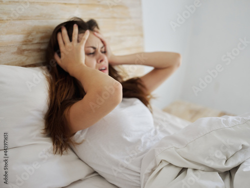 crying woman holding her head health problems lying in bed