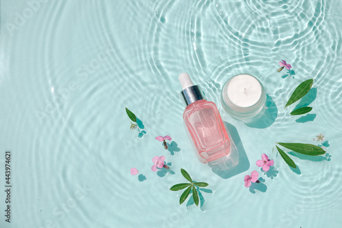 Moisturizing cosmetic products on water with drops. Serum glass bottle and cream jar on aqua surface Concept moisturizing summer beauty treatments