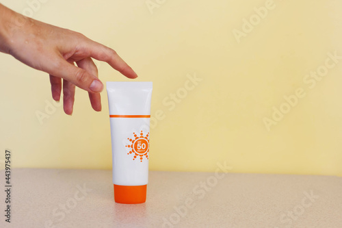 female hand touches a tube of sunscreen on a beige background . The concept of choosing maximum sun protection spf 50