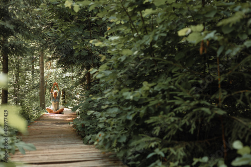 Young woman sits barefoot in forest and meditates, enjoys calmness and carelessness. Outdoor recreation and yoga concept