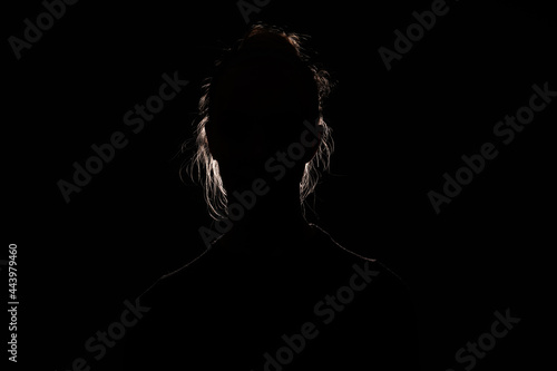 backlit portrait silhouette of unrecognizable woman hiding face and identy in the dark shadow