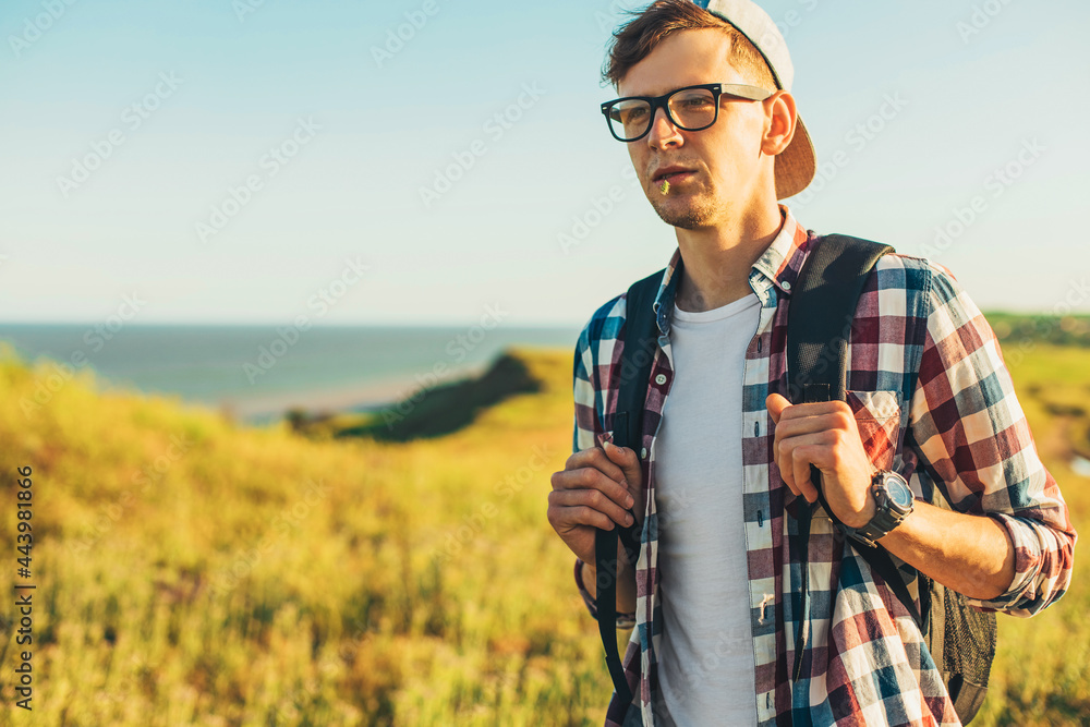 young man, in glasses and in a cap with a backpack, hiking and enjoying the mountain landscape, adventure man hiking in the desert mountains