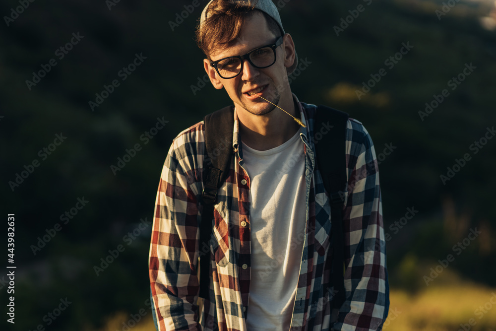 Young smiling man, in a cap with a backpack, hiking in the countryside, Relaxed handsome courageous young man in the wild forest