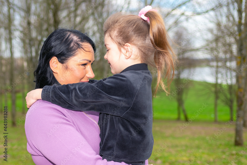 Beautiful mother and daughter play hugs in a spring park nature in profile looking at each other. Beautiful mother and daughter play hugs in a spring park nature in profile looking at each other.
