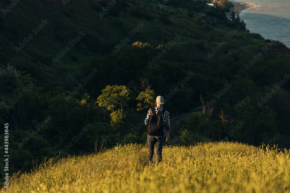 Male traveler, with a backpack, looks at the amazing mountains and forest, man on a country walk, hiking in the countryside, travel concept Male traveler, with a backpack, looks at the amazing mountains and forest, man on a country walk, hiking in the countryside, travel concept