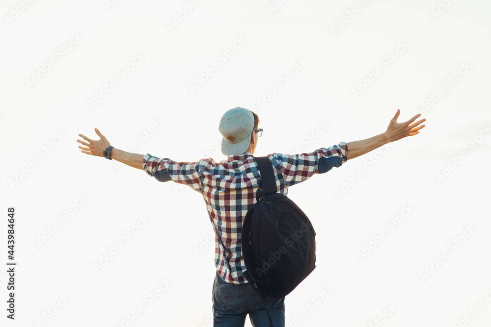Young man with a backpack standing with raised hands on the top of the mountain, against the background of blue sky Young man with a backpack standing with raised hands on the top of the mountain, against the background of blue sky