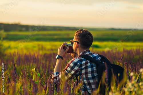 Young male tourist, in sunglasses, with a camera, in nature, spending time in a hike, on the field