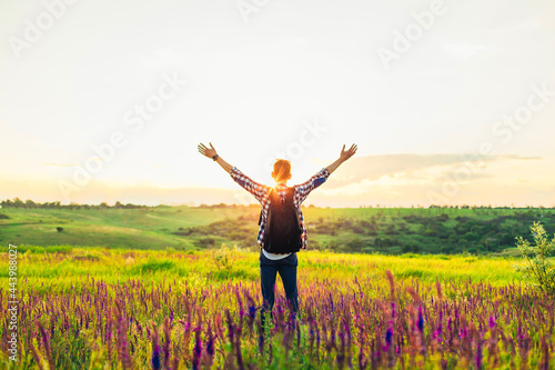 Traveler with raised hands standing on a hill in green grass and enjoying a majestic sunset, Successful man enjoying triumph