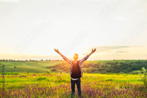 Traveler with raised hands standing on a hill in green grass and enjoying a majestic sunset, Successful man enjoying triumph